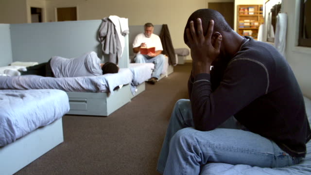 Depressed man sitting on bed in homeless shelter.Shot on Sony FS700 at frame rate of 25fps